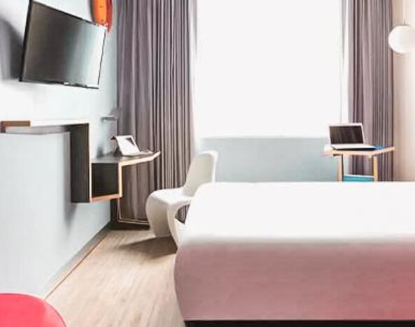 Guest room featuring a bed, workspace, wall-mounted television, contemporary furnishings, and colorful accent walls at Ibis Styles Mexico Reforma.