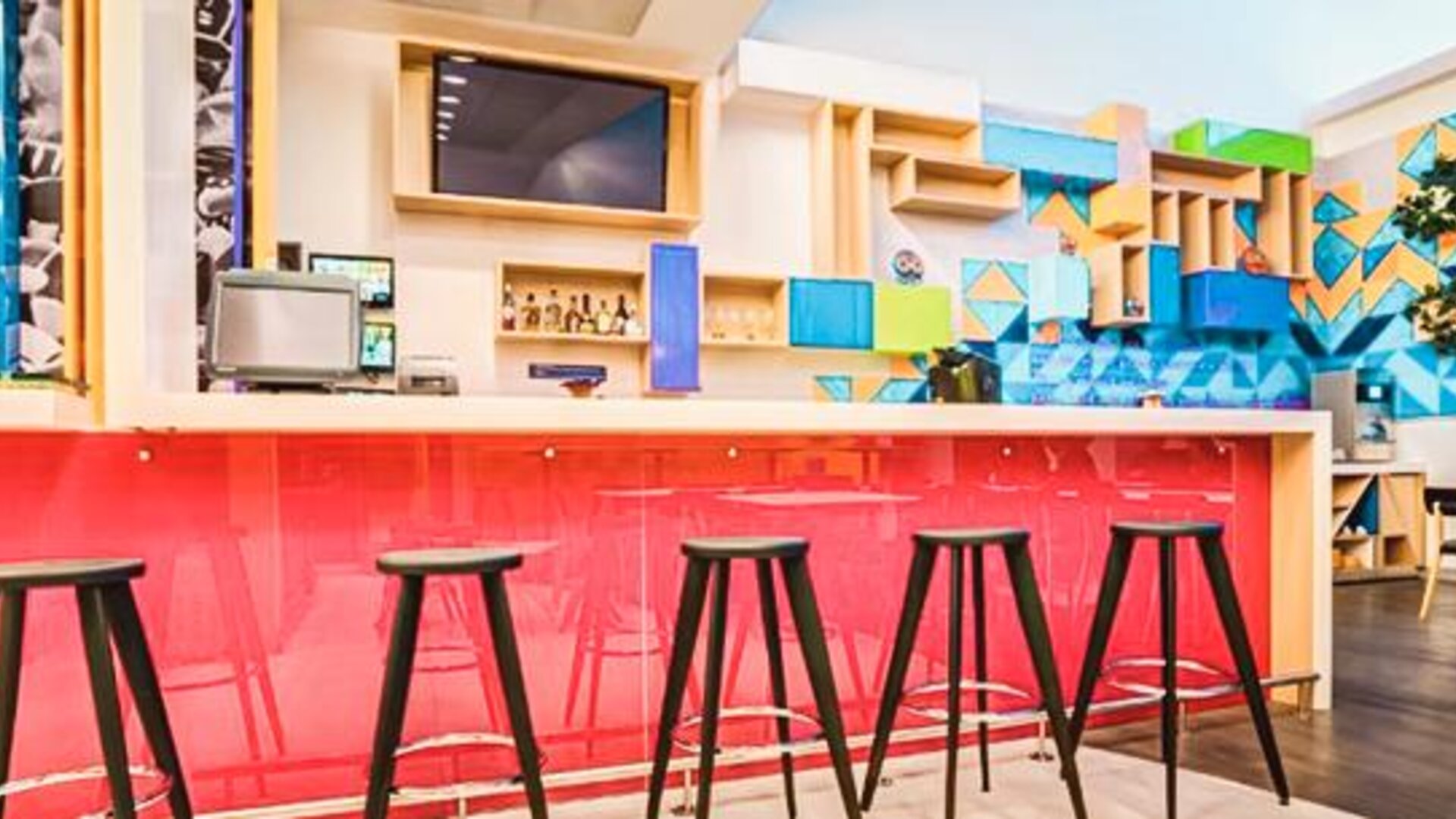 Hotel bar featuring high-top seating, a vibrant pink counter, geometric wall accents, and modern décor at Ibis Styles Mexico Reforma.