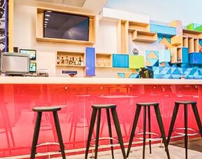 Hotel bar featuring high-top seating, a vibrant pink counter, geometric wall accents, and modern décor at Ibis Styles Mexico Reforma.