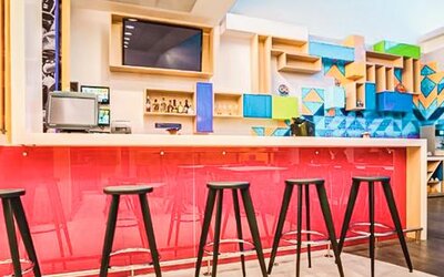 Hotel bar featuring high-top seating, a vibrant pink counter, geometric wall accents, and modern décor at Ibis Styles Mexico Reforma.