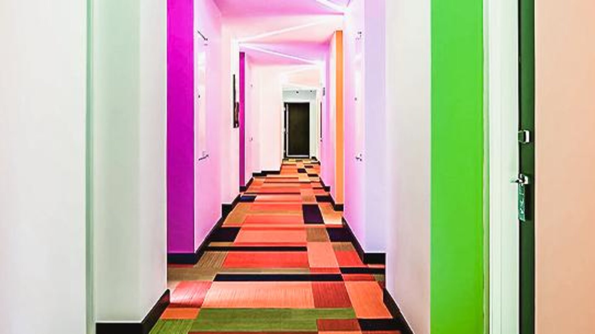 Bright hallway with colorful walls, patterned carpeting, and guest room entrances at Ibis Styles Mexico Reforma.