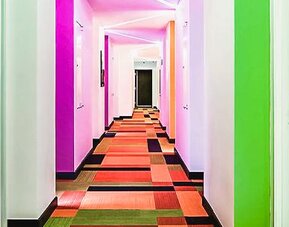 Bright hallway with colorful walls, patterned carpeting, and guest room entrances at Ibis Styles Mexico Reforma.