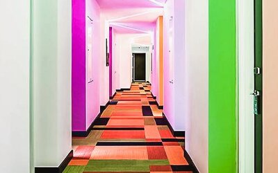 Bright hallway with colorful walls, patterned carpeting, and guest room entrances at Ibis Styles Mexico Reforma.