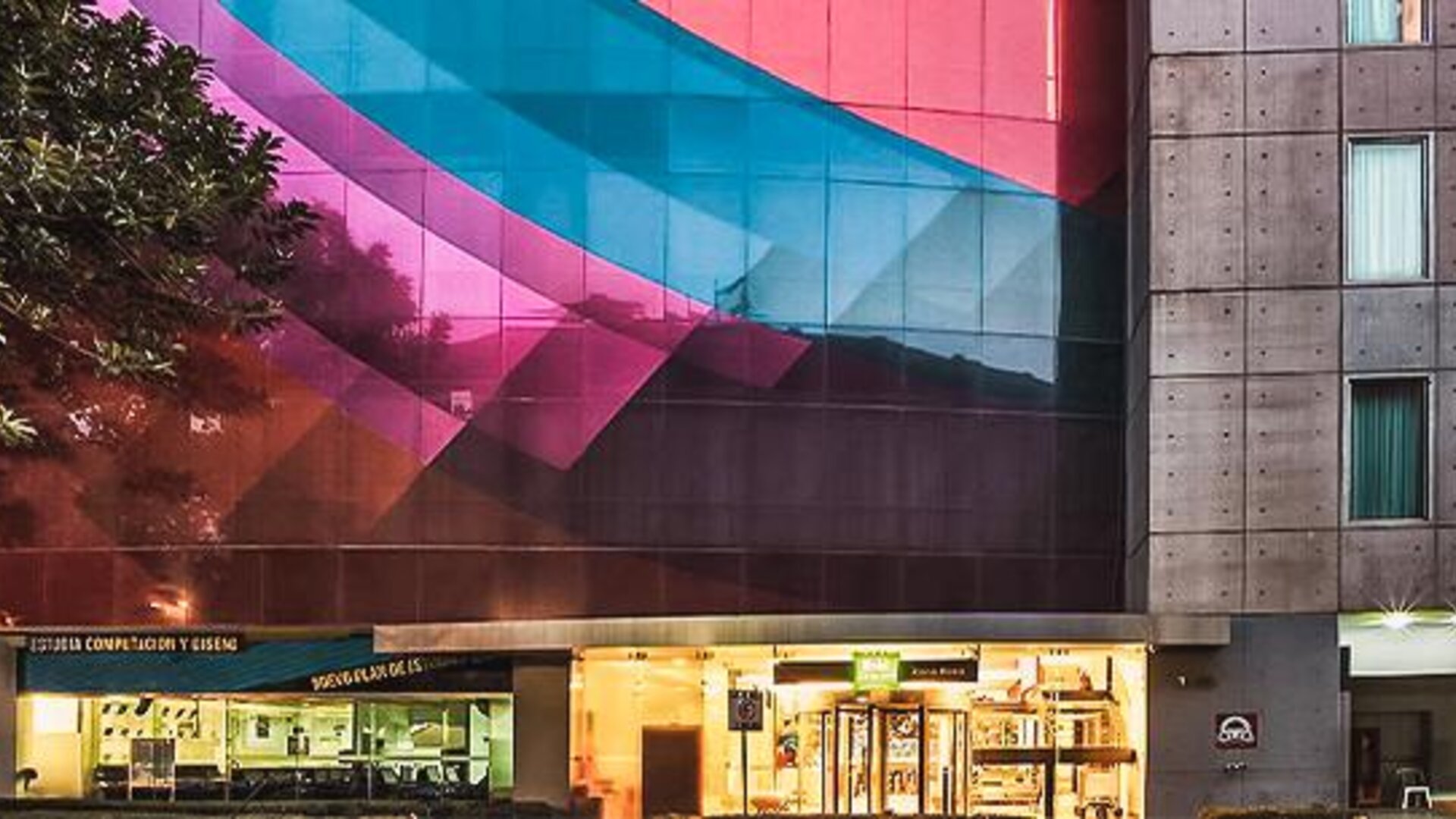 Exterior view of the hotel featuring a colorful geometric façade, modern architecture, and street-level storefronts at Ibis Styles Mexico Reforma.
