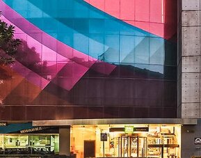 Exterior view of the hotel featuring a colorful geometric façade, modern architecture, and street-level storefronts at Ibis Styles Mexico Reforma.