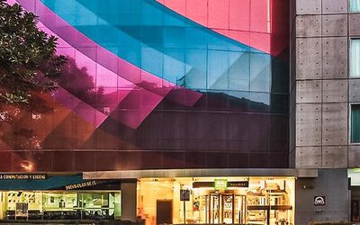 Exterior view of the hotel featuring a colorful geometric façade, modern architecture, and street-level storefronts at Ibis Styles Mexico Reforma.