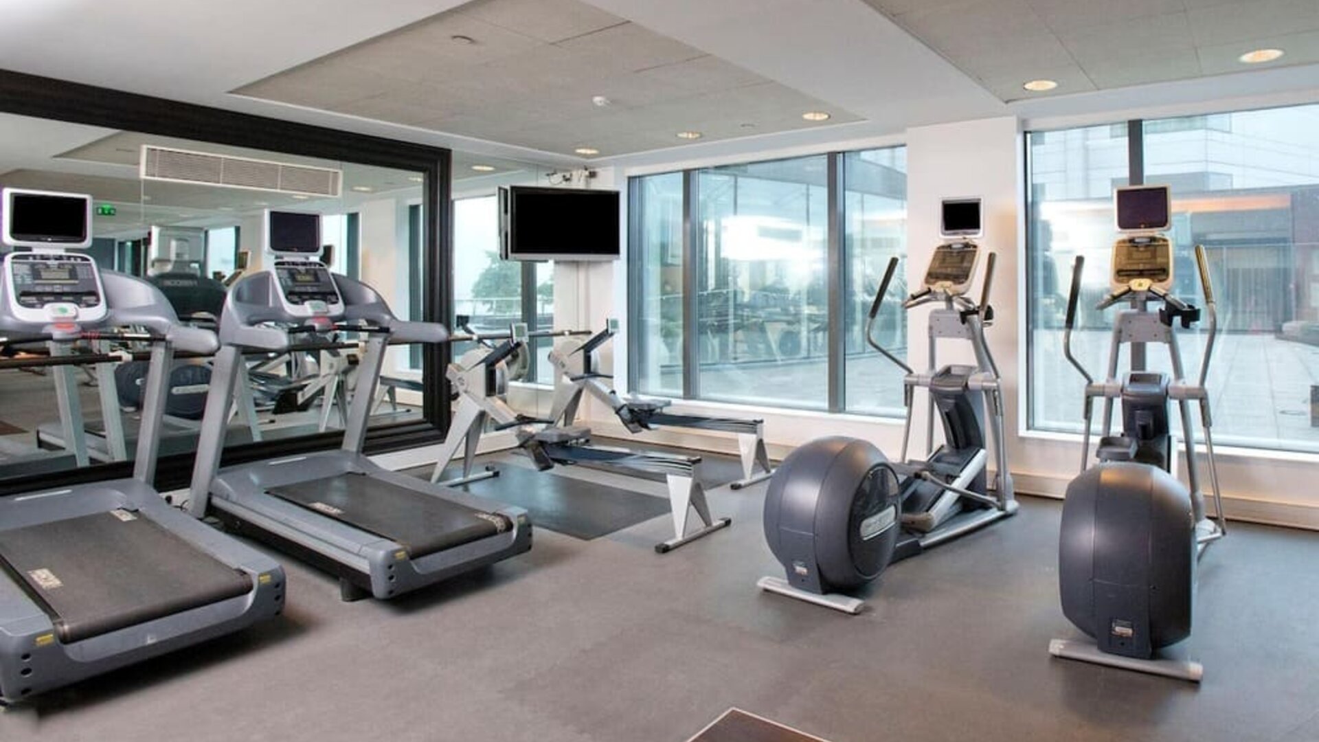 Hotel fitness center with treadmills, rowing machines, elliptical trainers, exercise bikes, mirrors and large windows.