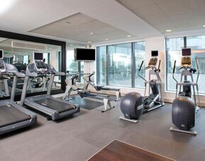 Hotel fitness center with treadmills, rowing machines, elliptical trainers, exercise bikes, mirrors and large windows.