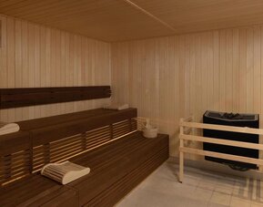 Wood-paneled hotel sauna with tiered wooden benches, folded towels, sauna heater and temperature gauges.