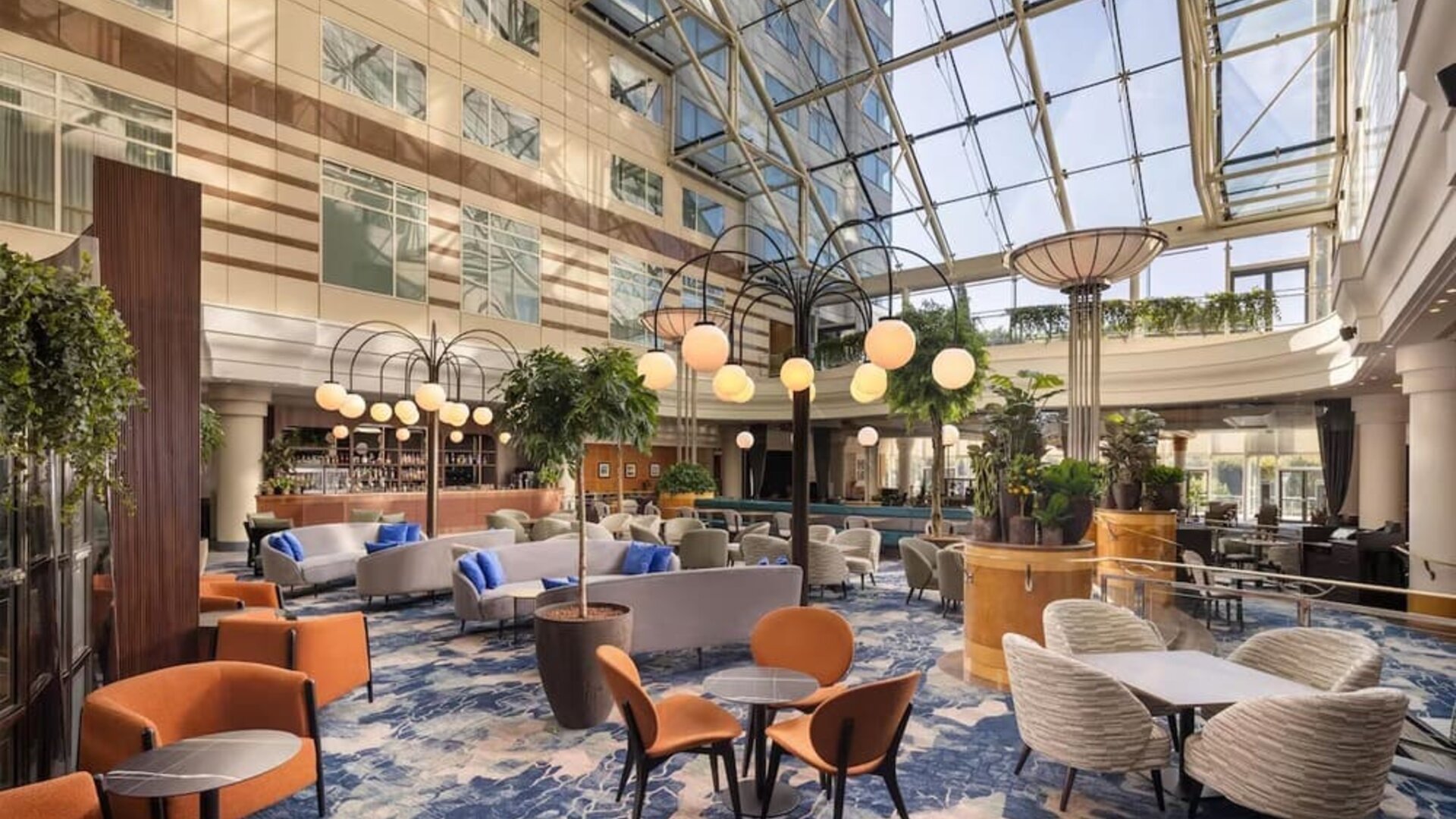 Contemporary hotel bar with upholstered lounge seating, wooden tables, globe pendant lights, plants and stocked bar.