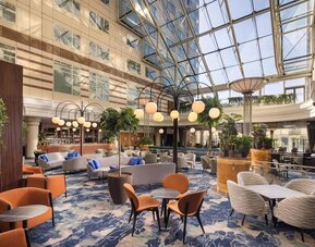 Contemporary hotel bar with upholstered lounge seating, wooden tables, globe pendant lights, plants and stocked bar.