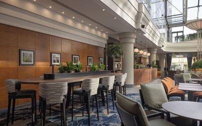Bright hotel coworking and lounge area with communal table, high chairs, comfortable seating and a glass atrium.