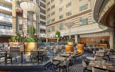 Large hotel atrium with restaurant tables, lounge seating, indoor trees, decorative columns and soaring glass ceiling