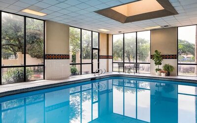 Indoor swimming pool featuring expansive windows, poolside seating, and a bright recreational space at Houston Marriott South at Hobby Airport.