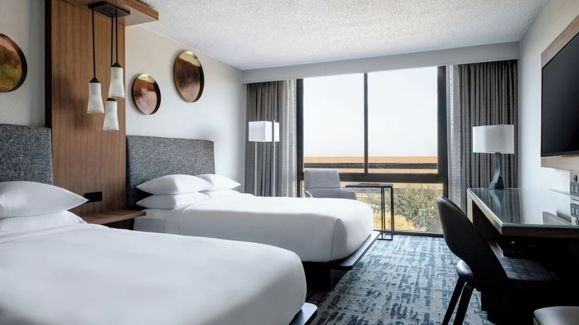 Guest room featuring two beds, floor-to-ceiling windows, a dedicated workspace, and contemporary furnishings at Houston Marriott South at Hobby Airport.