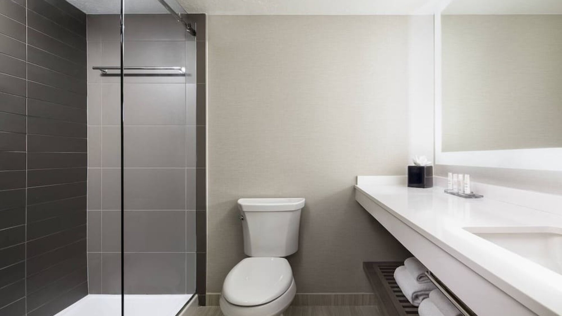 Bathroom featuring a walk-in shower, illuminated vanity, and contemporary fixtures at Houston Marriott South at Hobby Airport.