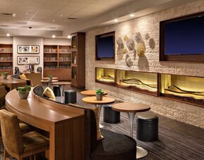 Lobby lounge featuring communal worktables, comfortable seating, built-in shelving, and a contemporary gathering space at Houston Marriott South at Hobby Airport.