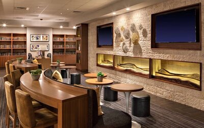 Lobby lounge featuring communal worktables, comfortable seating, built-in shelving, and a contemporary gathering space at Houston Marriott South at Hobby Airport.