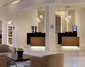 Reception area featuring illuminated check-in desks, modern lighting, and convenient access to hotel amenities at Houston Marriott South at Hobby Airport.