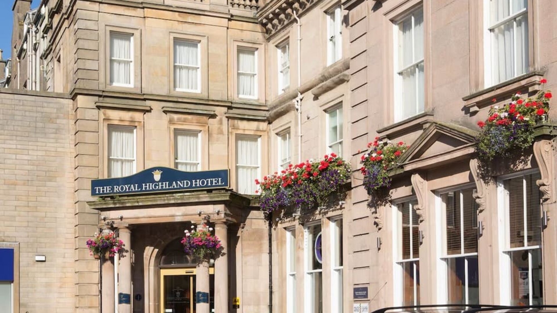 Historic hotel exterior featuring stone architecture, decorative flower displays, and the main entrance to The Royal Highland Hotel.