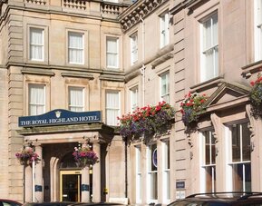 Historic hotel exterior featuring stone architecture, decorative flower displays, and the main entrance to The Royal Highland Hotel.