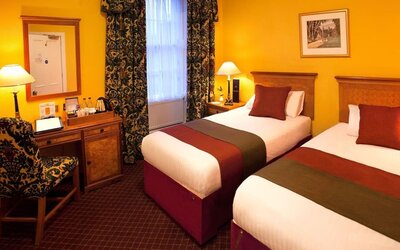 Guest room featuring two single beds, a writing desk, traditional décor, and warm-toned furnishings at The Royal Highland Hotel.