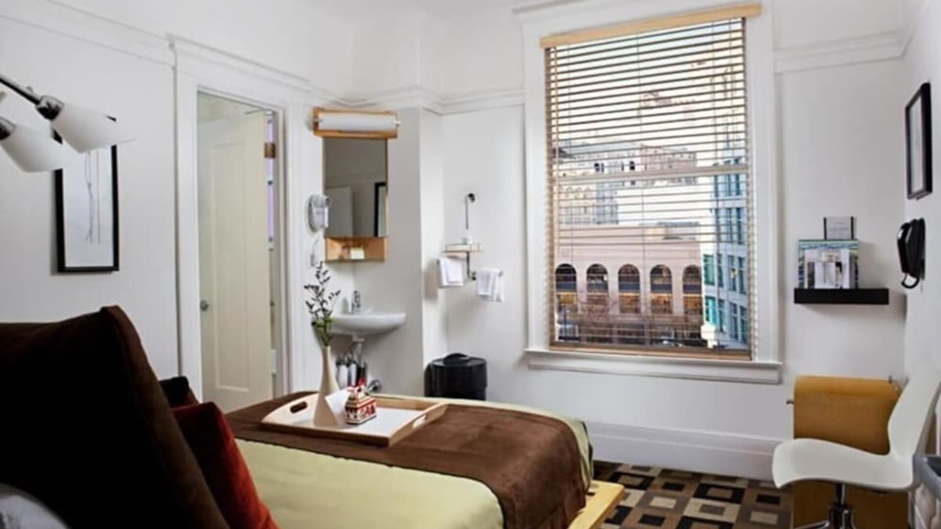 Guest room featuring large windows with city views, a writing desk, an open vanity area, and contemporary furnishings at The Mosser Hotel.