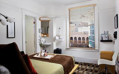 Guest room featuring large windows with city views, a writing desk, an open vanity area, and contemporary furnishings at The Mosser Hotel.
