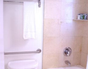 Bathroom featuring a combination bathtub and shower, stone tile walls, chrome fixtures, and neatly arranged towels at The Mosser Hotel.