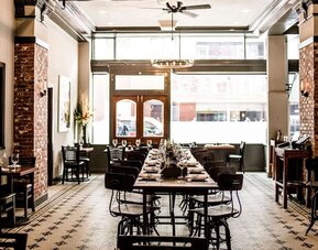 Restaurant featuring exposed brick walls, communal dining tables, high ceilings, and an industrial-inspired design at The Mosser Hotel.