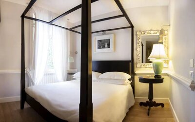 Guest room featuring a four-poster bed, hardwood flooring, sheer curtains, and elegant furnishings at Cellai Boutique Hotel.