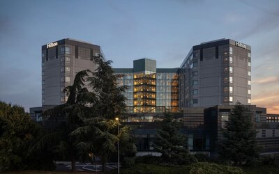 Hotel exterior at dusk with trees and garden setting. 
