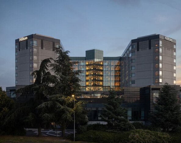 Hotel exterior at dusk with trees and garden setting. 