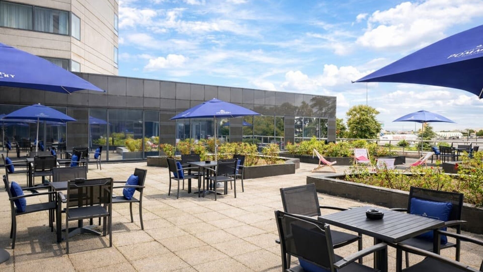 Hotel outdoor terrace with tables, chairs, landscaped planters and open views toward the nearby airport.