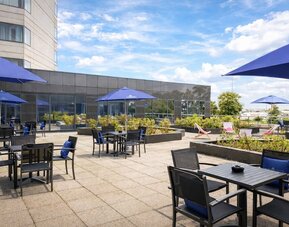 Hotel outdoor terrace with tables, chairs, landscaped planters and open views toward the nearby airport.