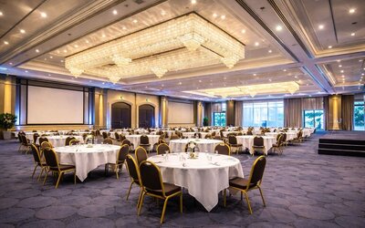 Hotel conference room with round conference tables, chairs, presentation screen, and natural light. 
