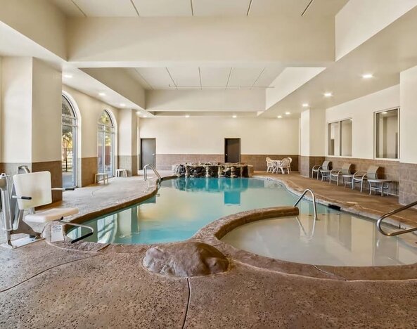 Indoor swimming pool and adjacent whirlpool spa with accessible entry and waterfall features at Comfort Suites Frisco.