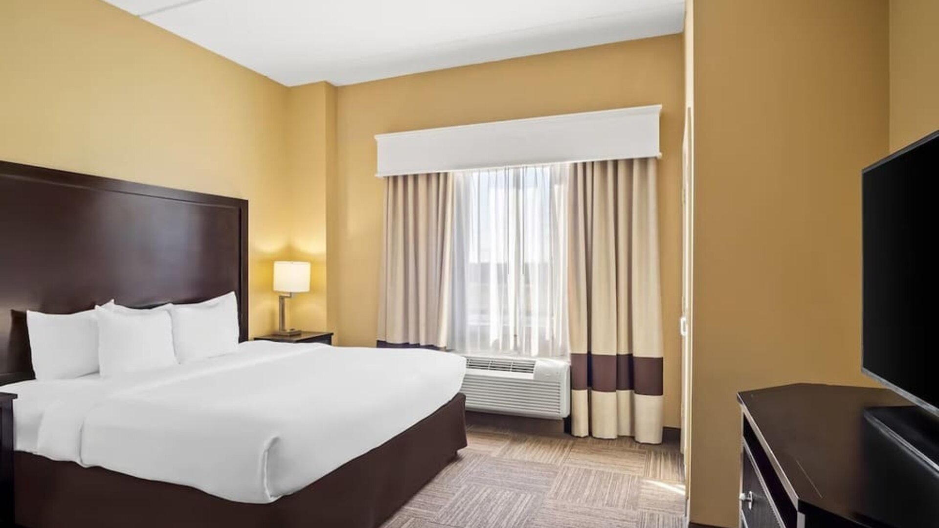 Guest room with a king-size bed, work desk, flat-screen television, and large window with blackout curtains at Comfort Suites Frisco.