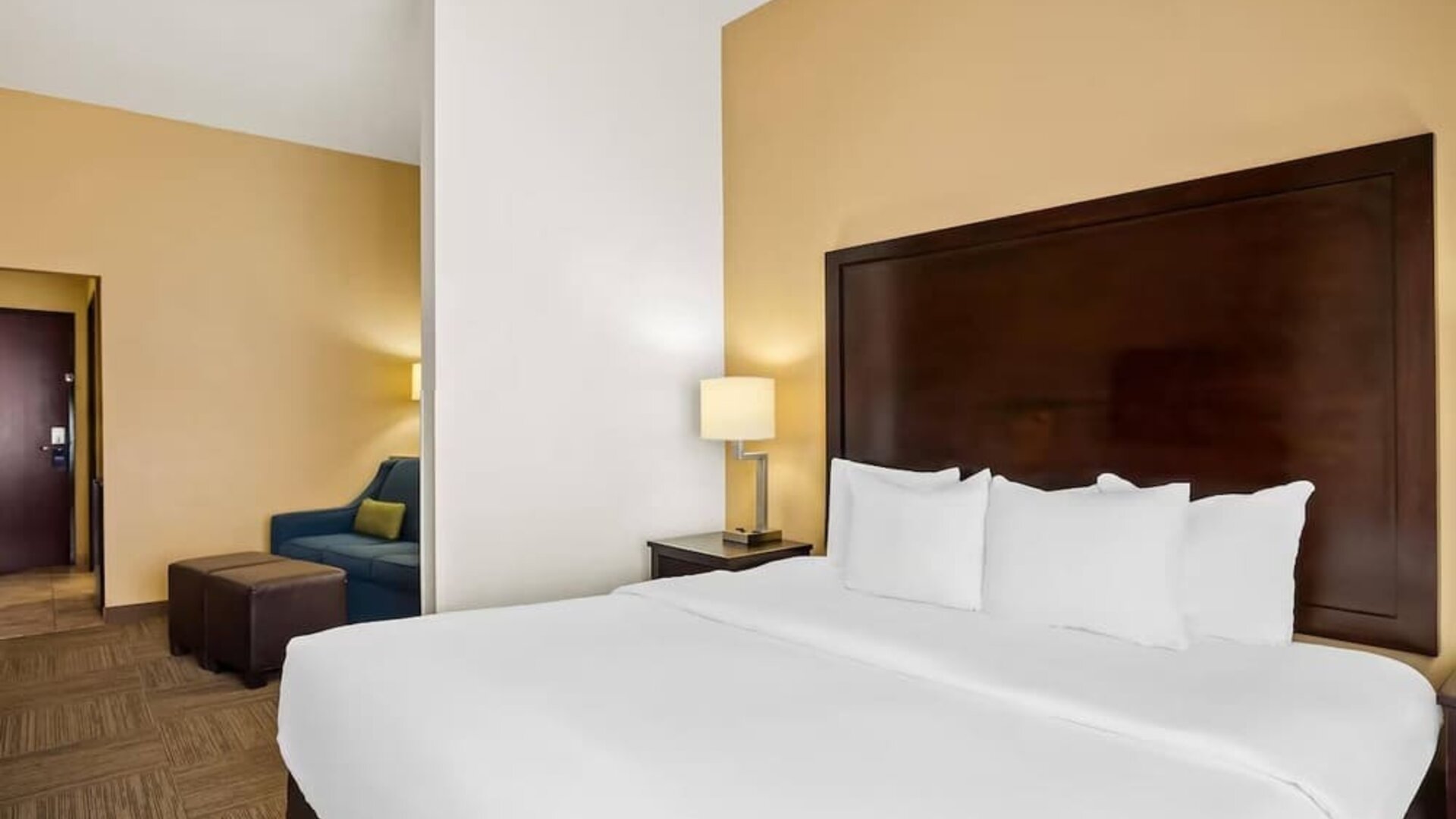 King guest room with a separate sitting area, sofa, ottomans, and bedside lighting at Comfort Suites Frisco.