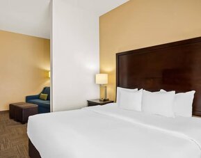 King guest room with a separate sitting area, sofa, ottomans, and bedside lighting at Comfort Suites Frisco.