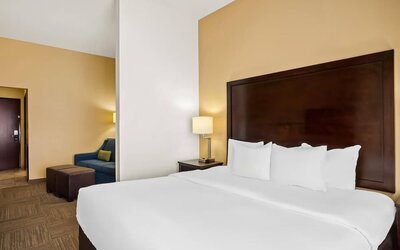 King guest room with a separate sitting area, sofa, ottomans, and bedside lighting at Comfort Suites Frisco.