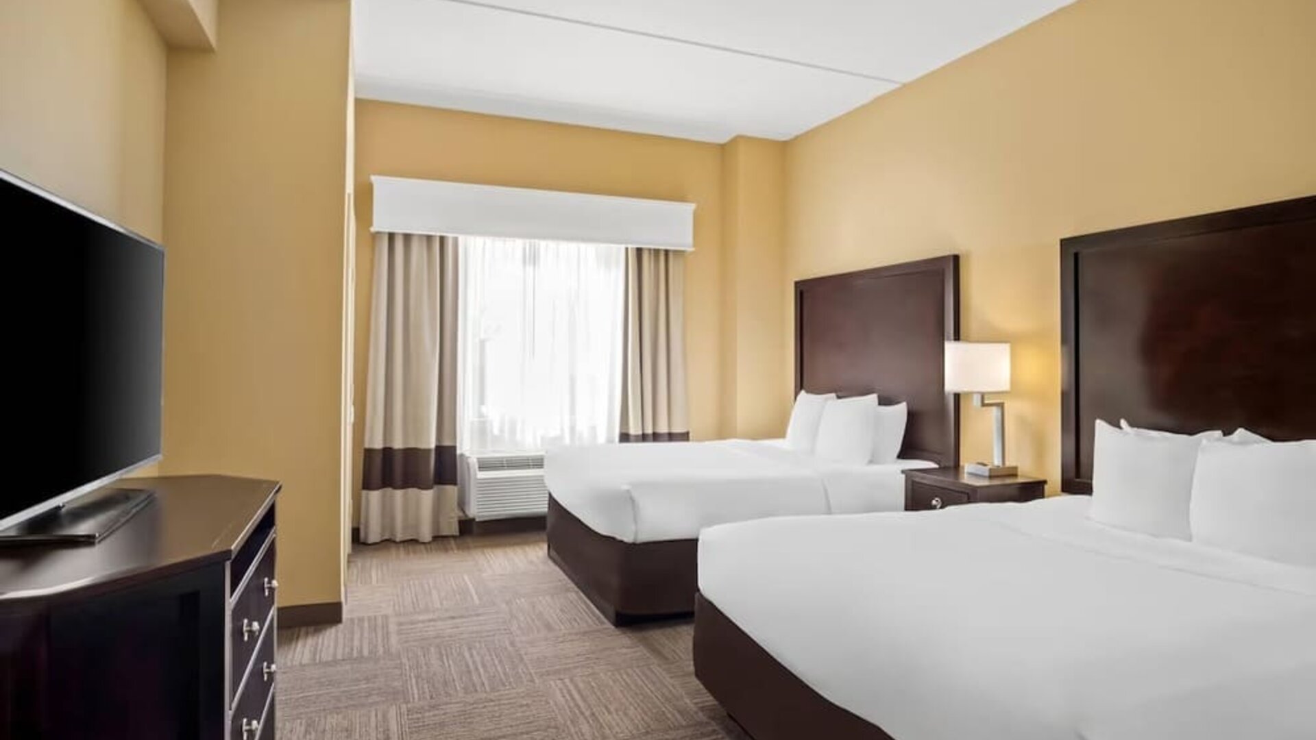 Guest room with two queen beds, a work desk, dresser, and large window providing natural light at Comfort Suites Frisco.