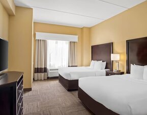 Guest room with two queen beds, a work desk, dresser, and large window providing natural light at Comfort Suites Frisco.
