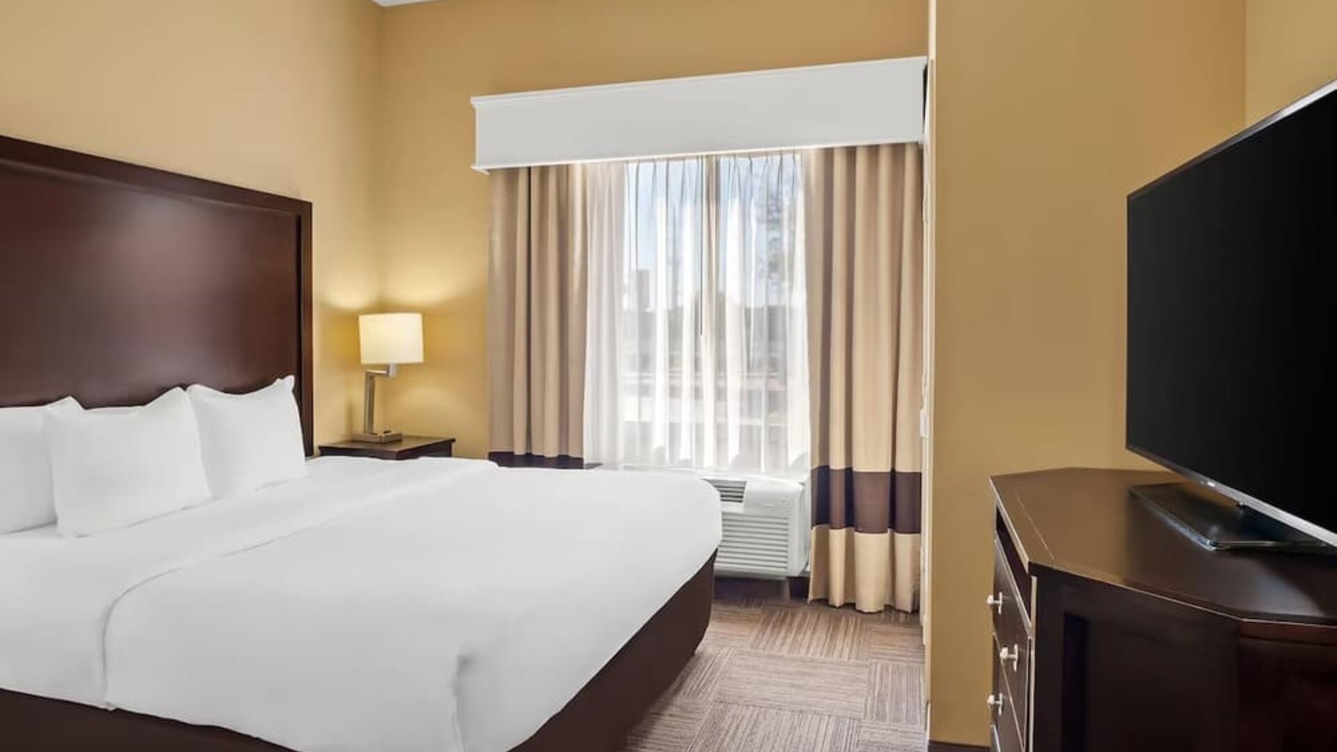 Standard king room with a flat-screen television, dresser, bedside table, and window seating area at Comfort Suites Frisco.