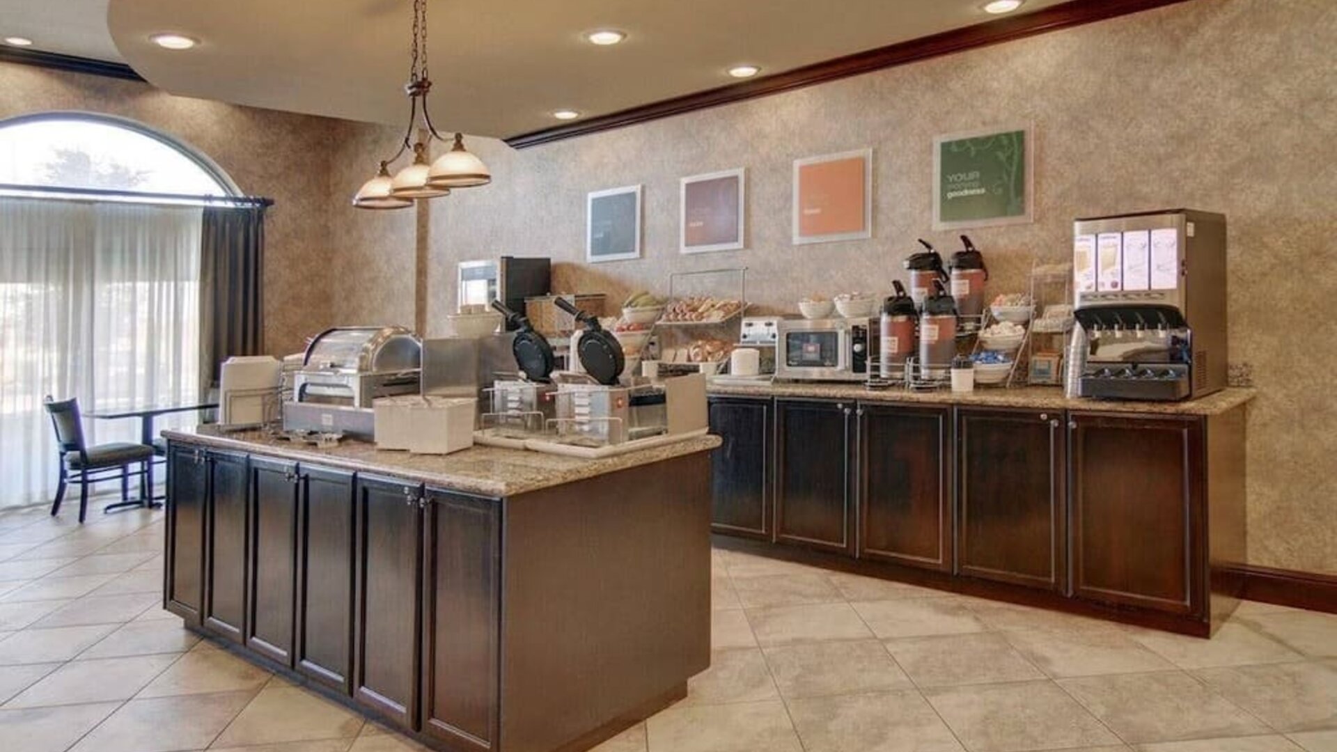 Complimentary breakfast area featuring hot breakfast stations, cereal dispensers, coffee service, and self-serve dining options at Comfort Suites Frisco.