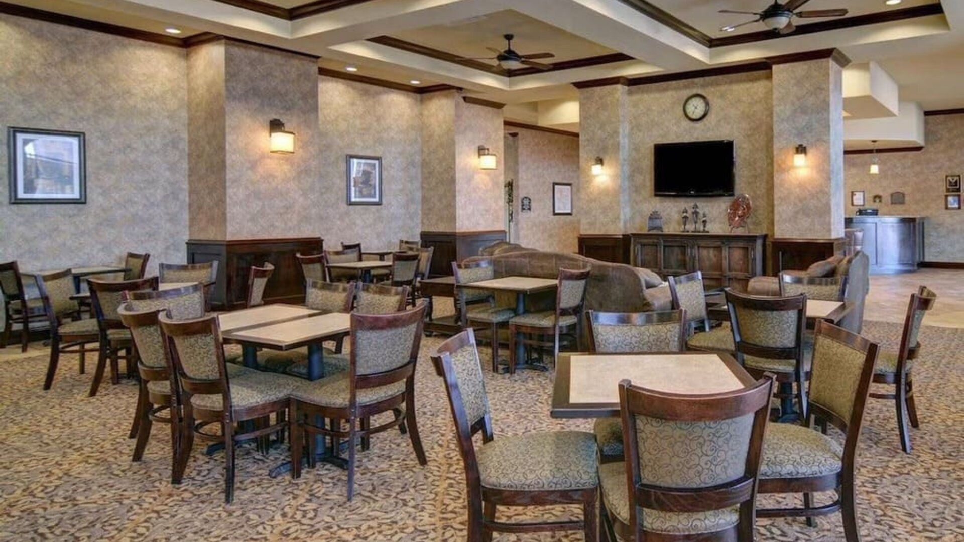 Spacious dining and lounge area with tables, upholstered seating, a television, and a fireplace at Comfort Suites Frisco.