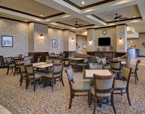 Spacious dining and lounge area with tables, upholstered seating, a television, and a fireplace at Comfort Suites Frisco.
