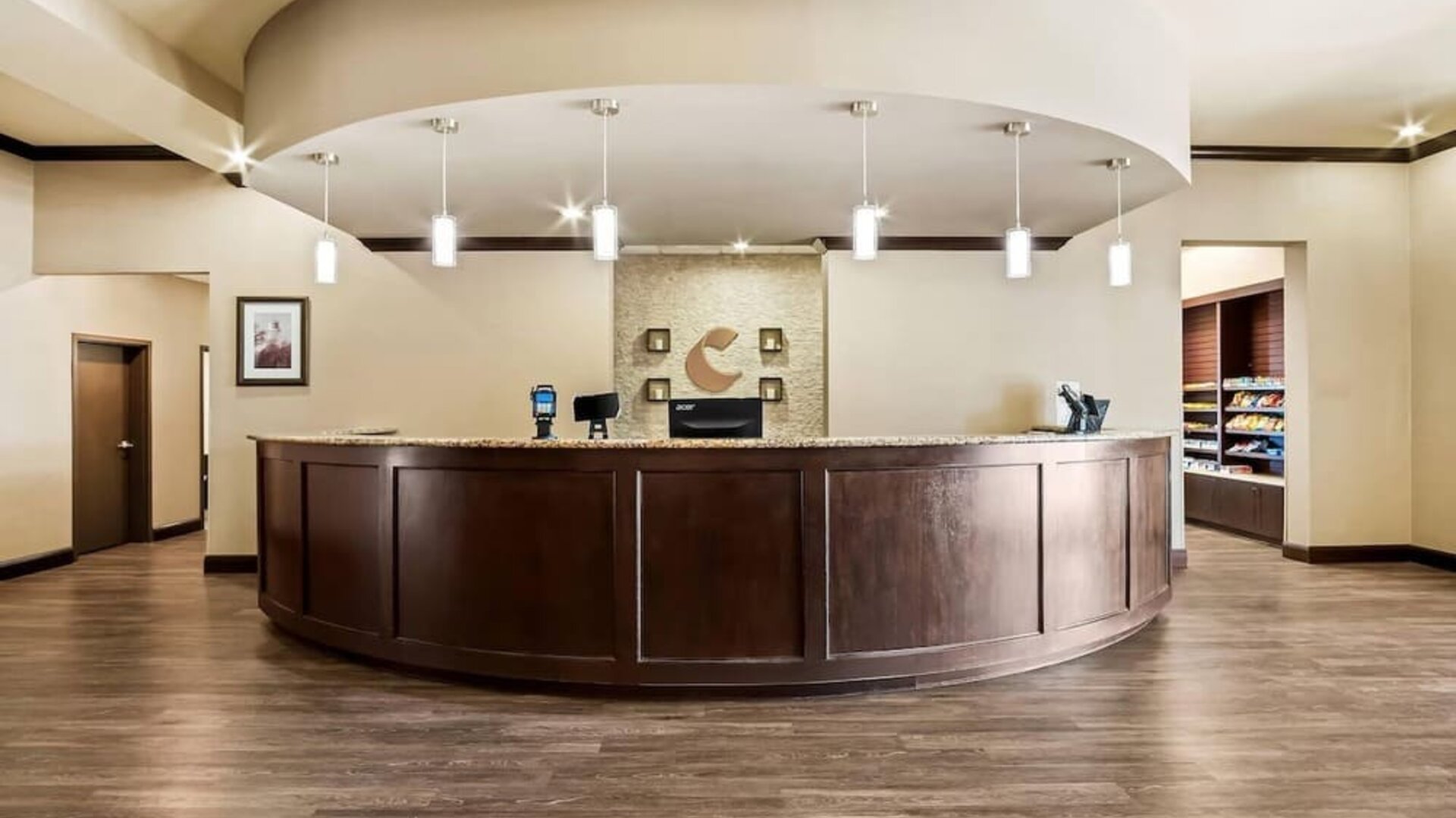 Reception desk with a curved granite counter, pendant lighting, and a convenient snack market at Comfort Suites Frisco.