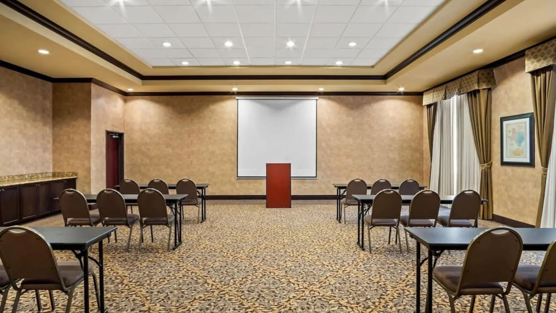 Meeting room arranged in a classroom-style layout with tables, chairs, a projection screen, and a presentation podium at Comfort Suites Frisco.