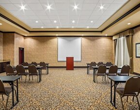 Meeting room arranged in a classroom-style layout with tables, chairs, a projection screen, and a presentation podium at Comfort Suites Frisco.
